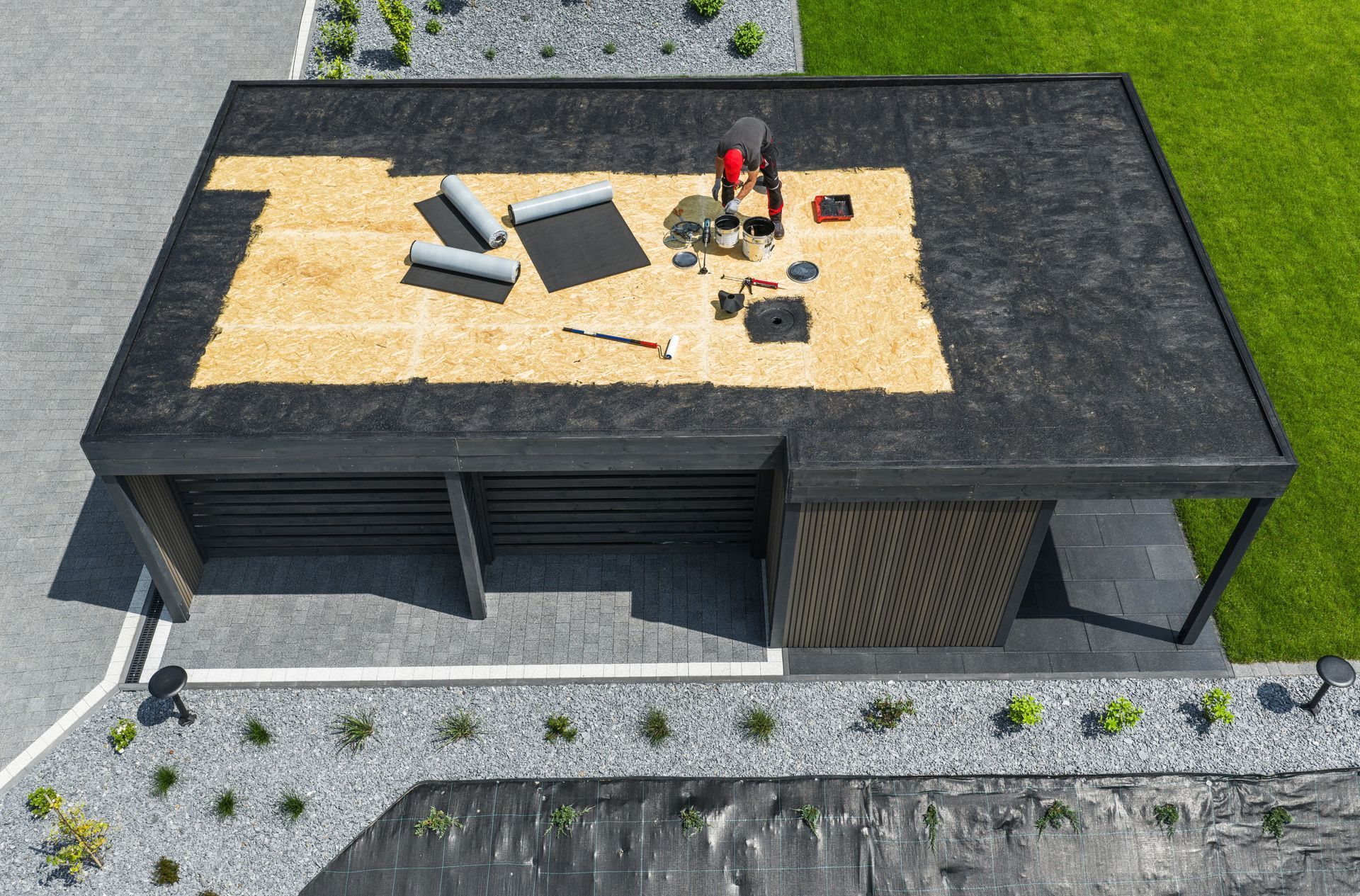 Aerial view of a house roof under repair, with exposed plywood, tools, and two workers on top.