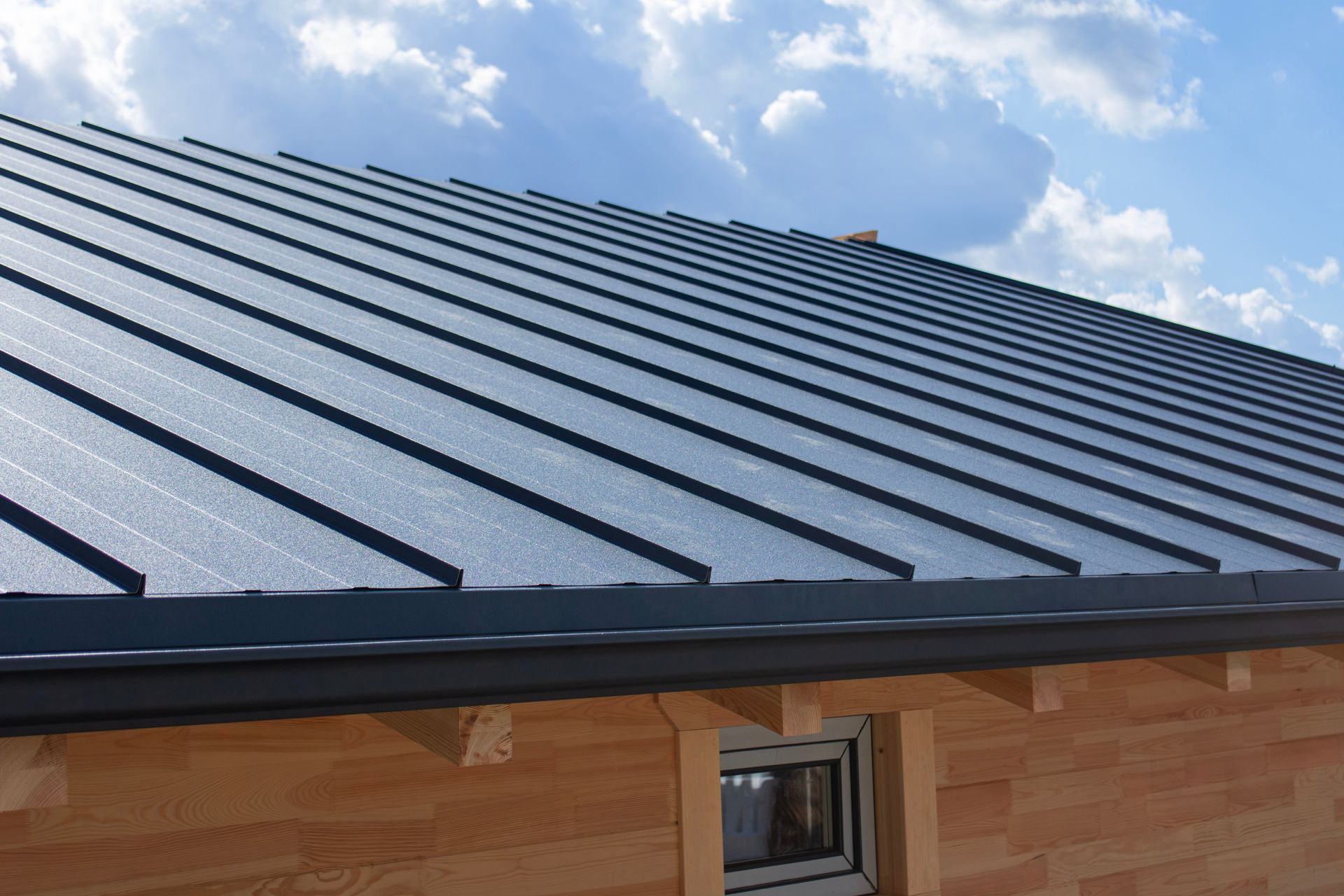 Dark metal roof on a wooden building under a blue sky with clouds