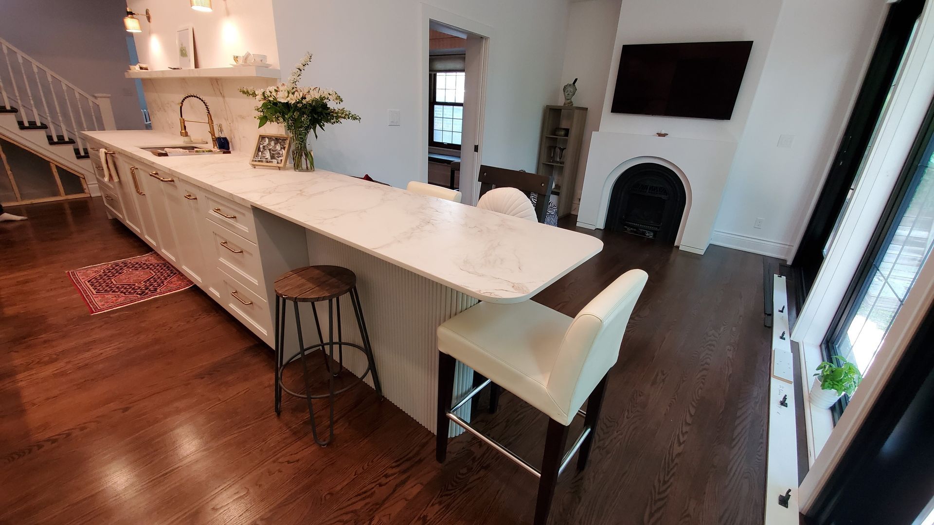 A kitchen with a long island , stools , a television and a fireplace.