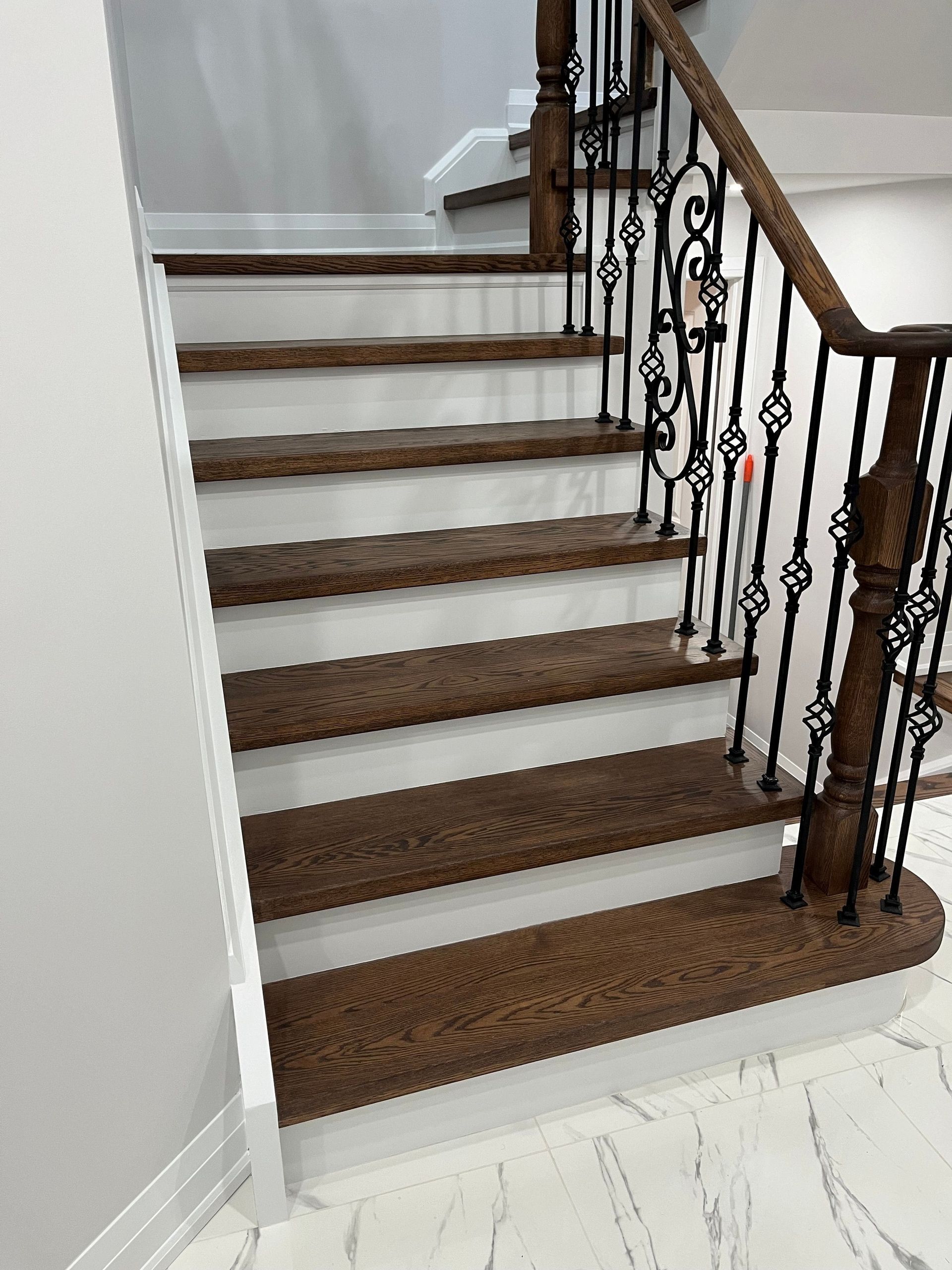 A wooden staircase with white steps and a wrought iron railing.