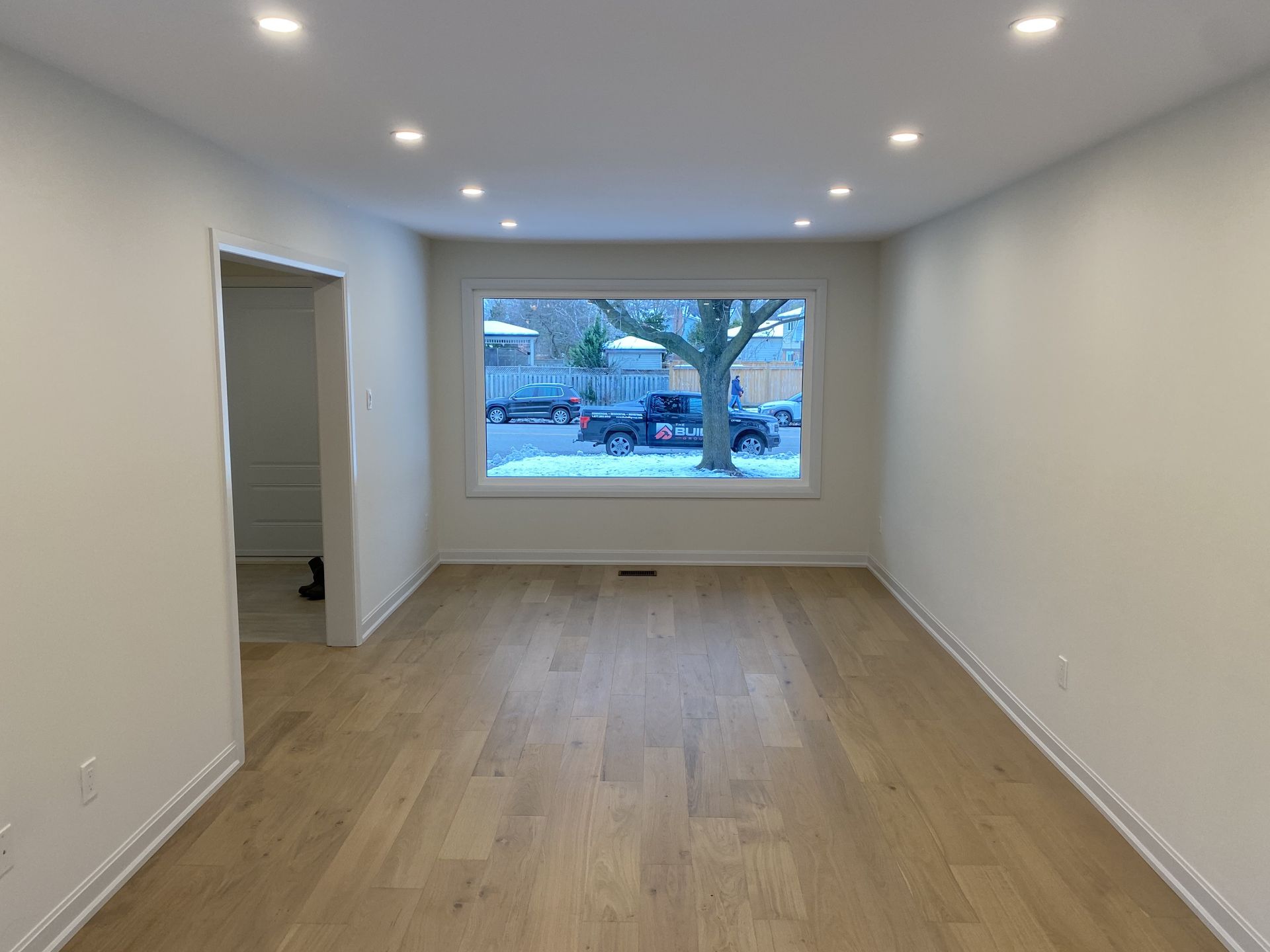 An empty living room with hardwood floors and a large window.