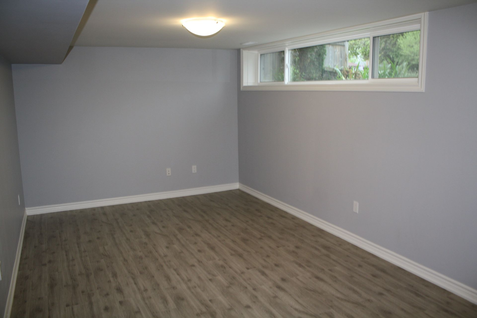 An empty basement with hardwood floors and a window.