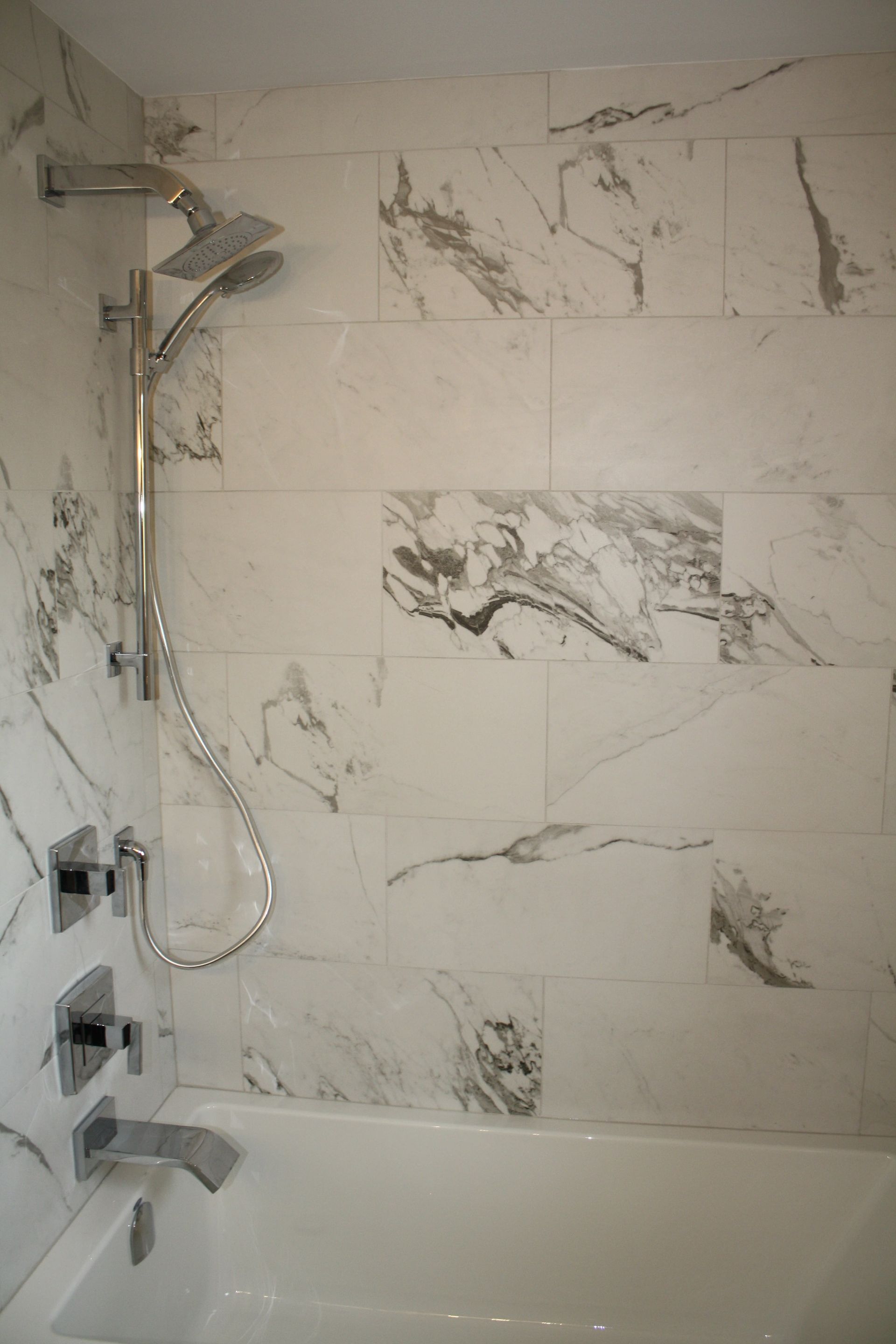 A bathroom with marble tiles , a tub and a shower.