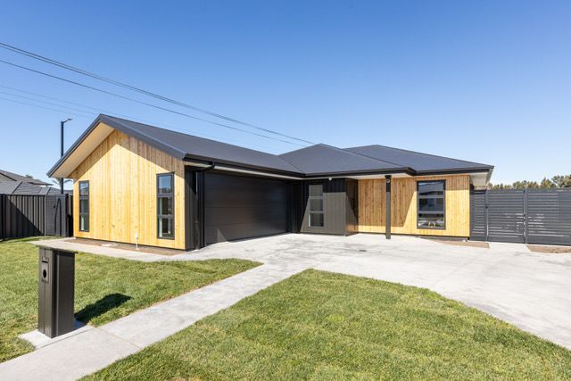 A house with a black roof and wooden siding is sitting on top of a lush green lawn.