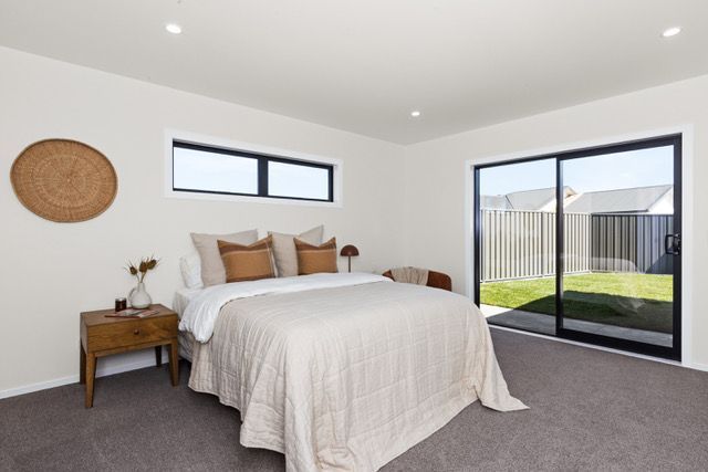 A bedroom with a large bed and a sliding glass door leading to the backyard.
