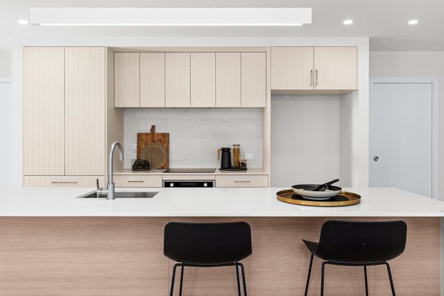A kitchen with white cabinets , a sink , and two chairs.