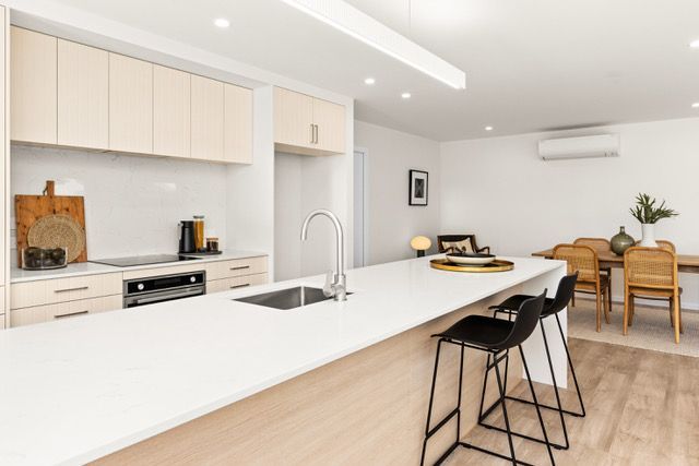 A kitchen with a large island and stools and a dining room in the background.