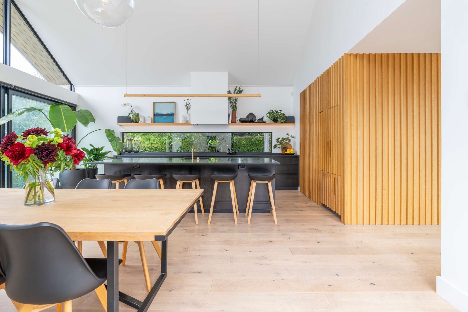A dining room with a table and chairs and a vase of flowers.