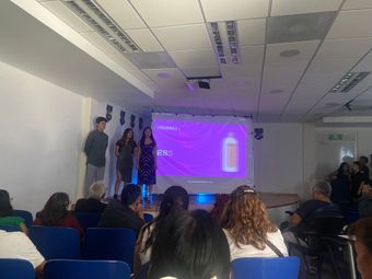 Tres personas en un escenario presentan sus productos ante el público. Una pantalla muestra la imagen de un producto.