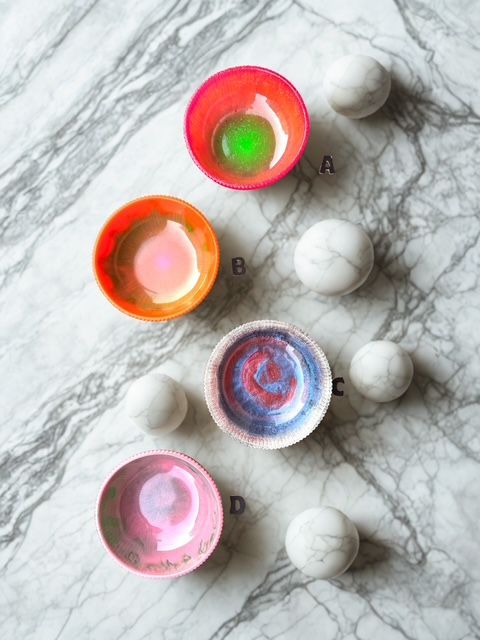 Four colorful bowls and white marble spheres arranged on a marble surface.