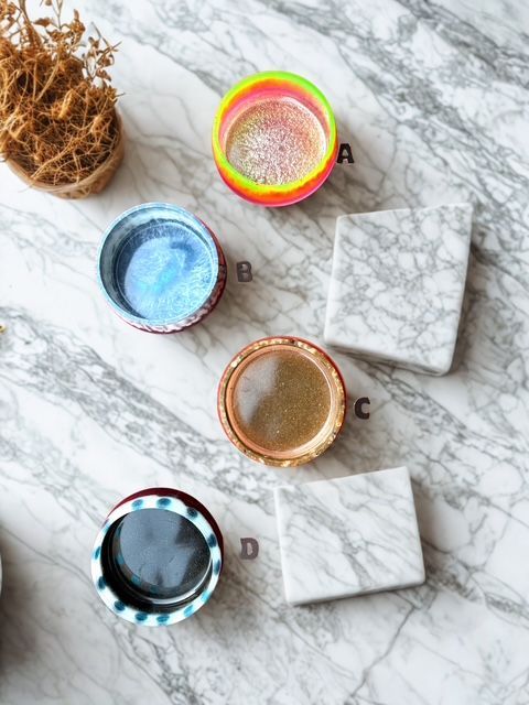 Four colorful glitter jars and marble coasters on a marble surface.