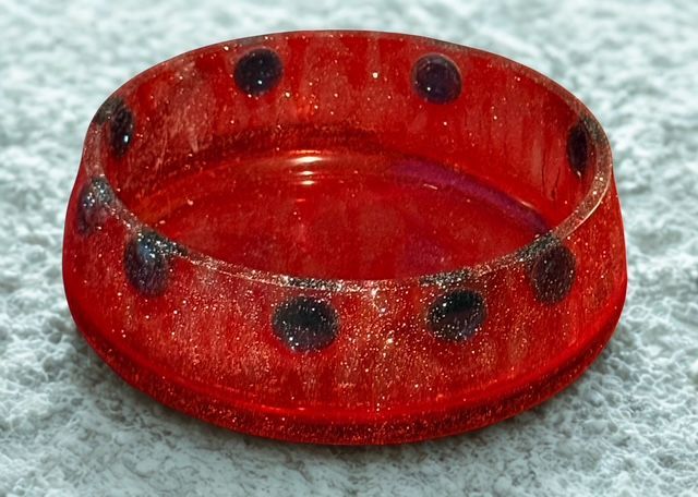 Red, circular bowl with dark spots around the rim.
