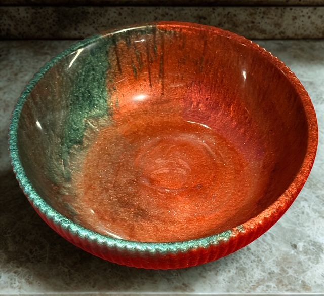 Ceramic bowl, red-orange interior with a green rim, textured details, sitting on a marbled surface.