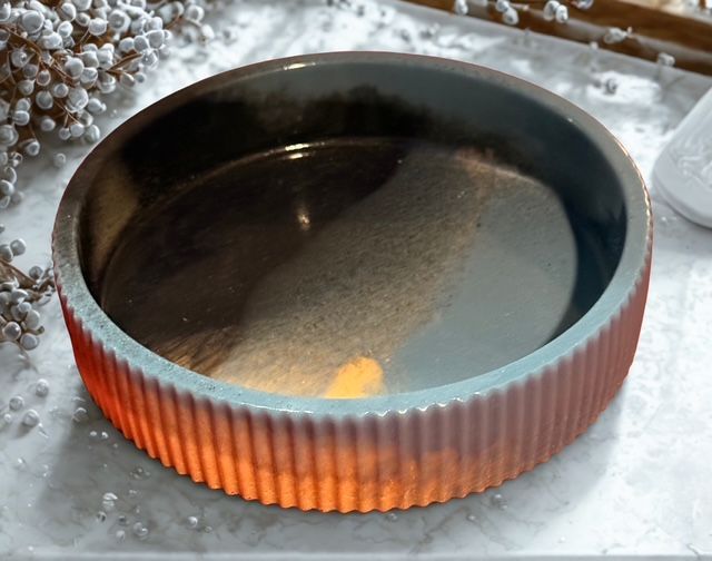 Ceramic bowl, red-brown with water inside, on a marble surface, near white flowers.