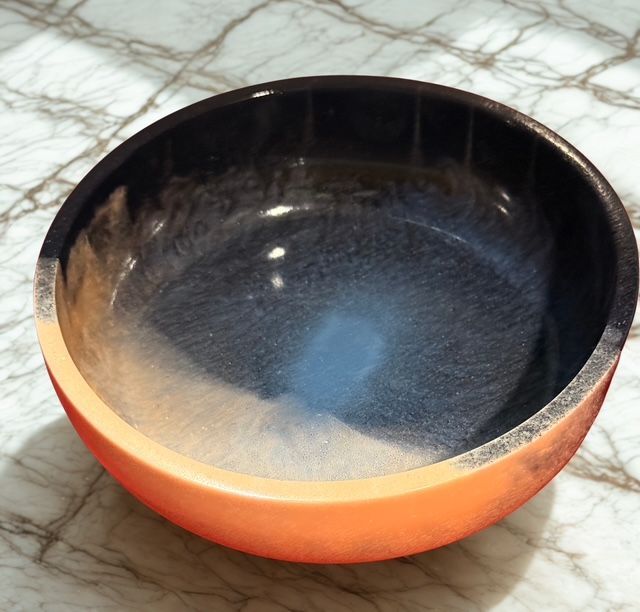 An orange bowl with a black rim sits on a marble surface