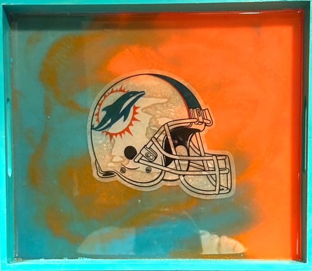 Miami Dolphins helmet on a resin tray with teal and orange swirls.