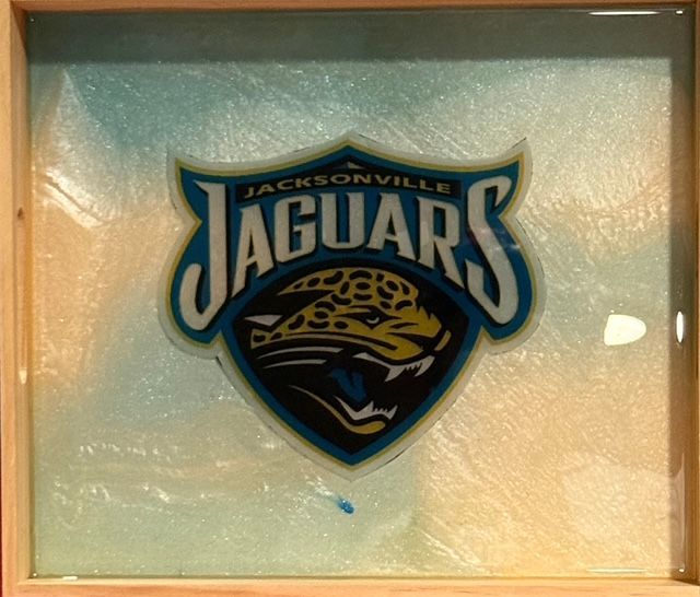Jacksonville Jaguars logo in a resin-covered wooden frame, with a blue, gold, and teal background.