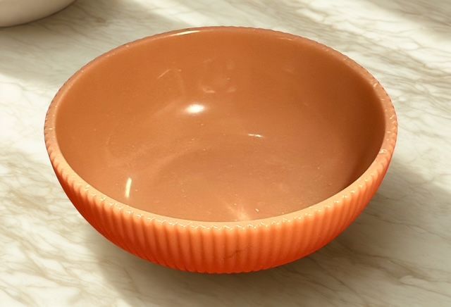 An orange bowl is sitting on a marble counter top
