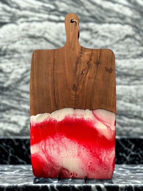 A wooden cutting board with a red and white design on it is sitting on a counter.