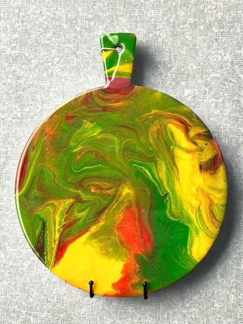 A green , yellow and red plate with a handle is hanging on a wall.