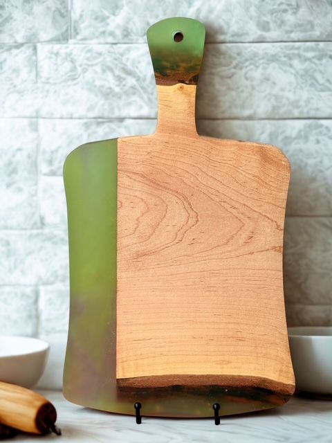 Wooden cutting board, olive green resin handle, resting on a black metal stand in front of a white tile wall.