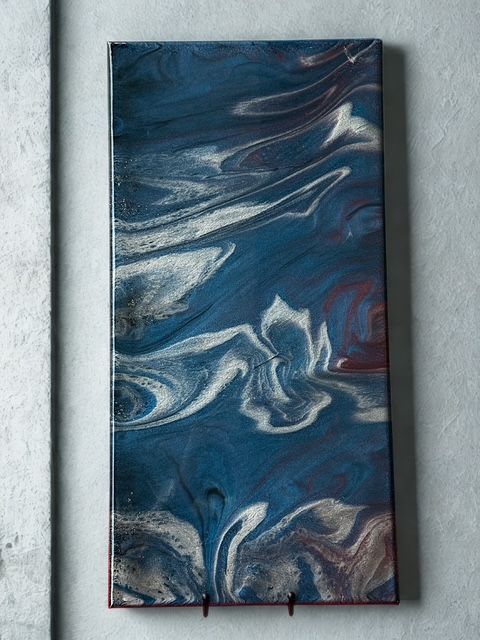 Abstract blue and white artwork on a rectangular board, mounted on a gray wall.
