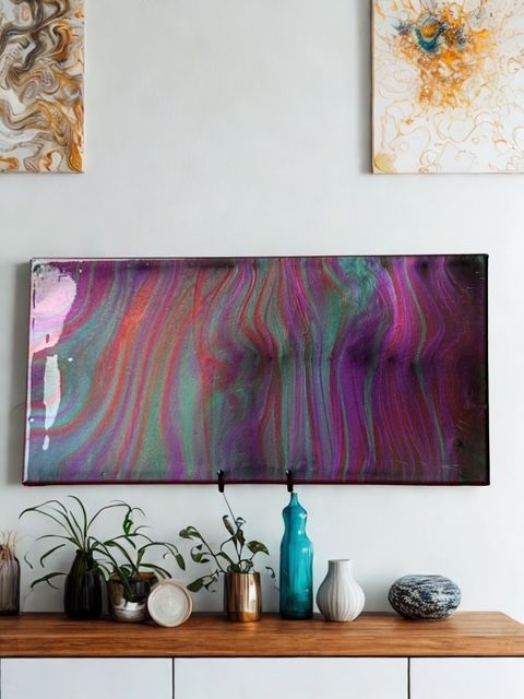 Abstract art piece with vibrant pink, purple, and green swirls, mounted above a wooden console with plants and decorative vases.