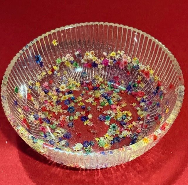 A clear glass bowl filled with colorful flowers on a red surface