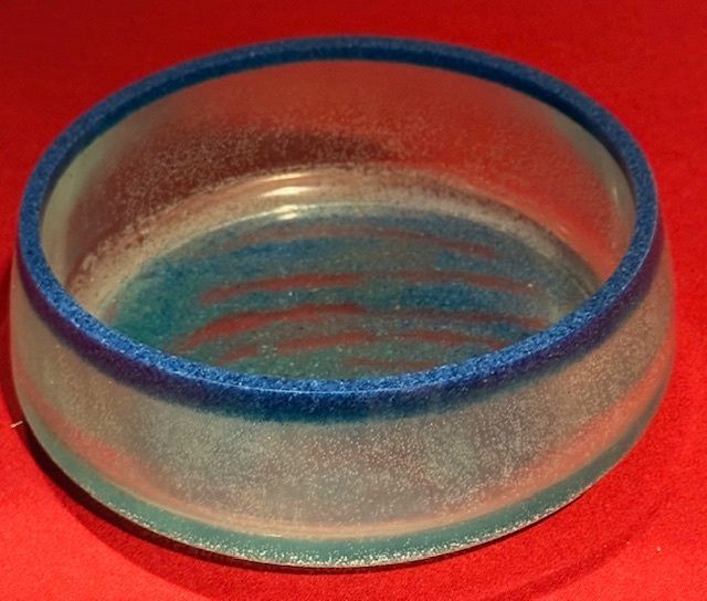 A clear bowl with a blue rim sits on a red surface