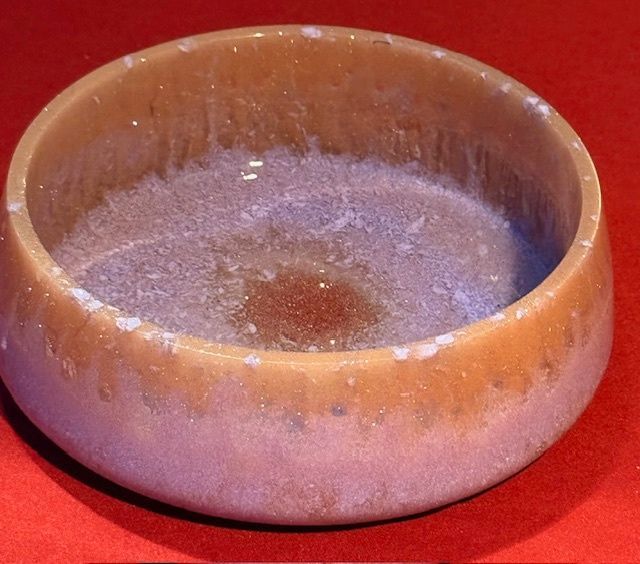 A bowl with a purple liquid in it sits on a red surface