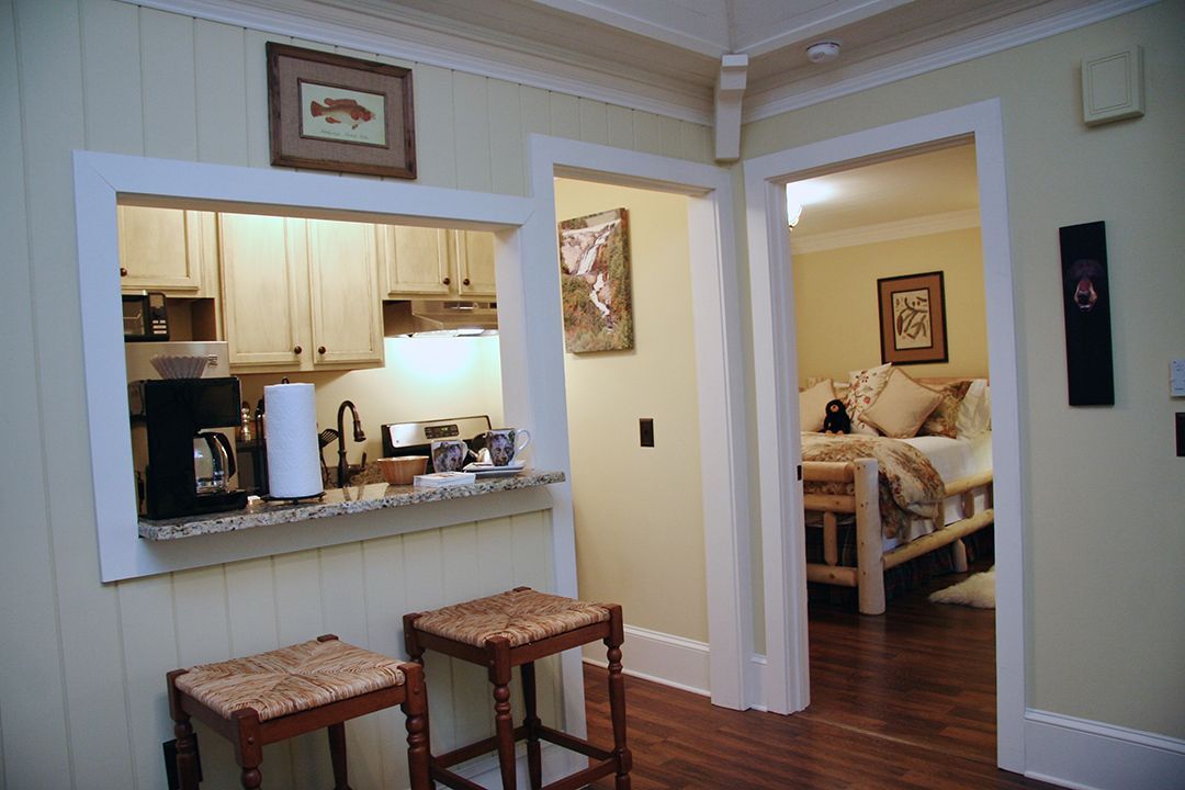 A kitchen with a counter and stools and a living room in the background
