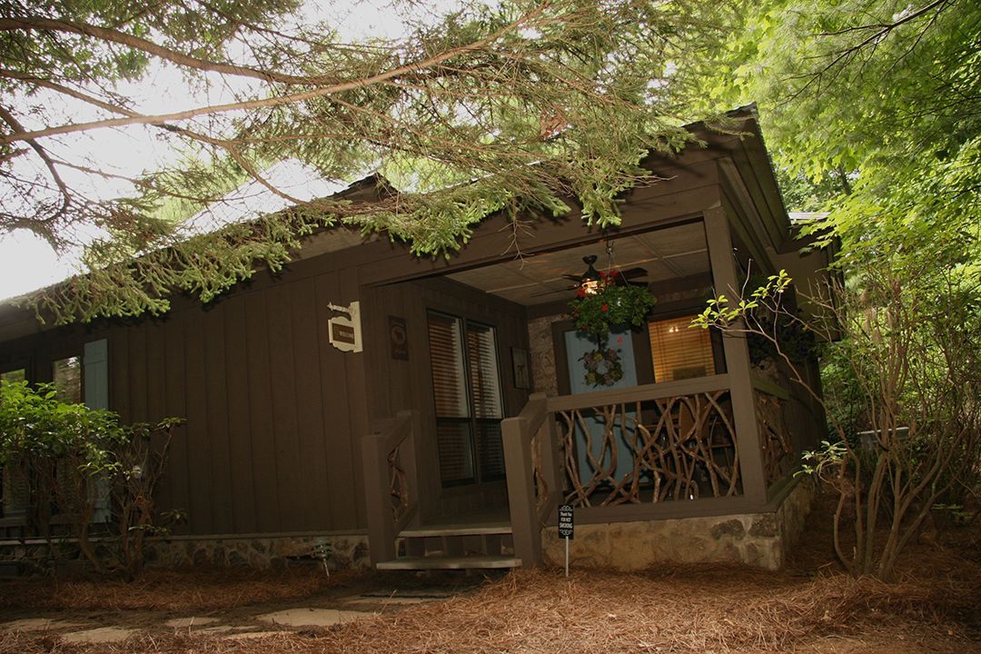 A small brown house with a porch in the middle of a forest.