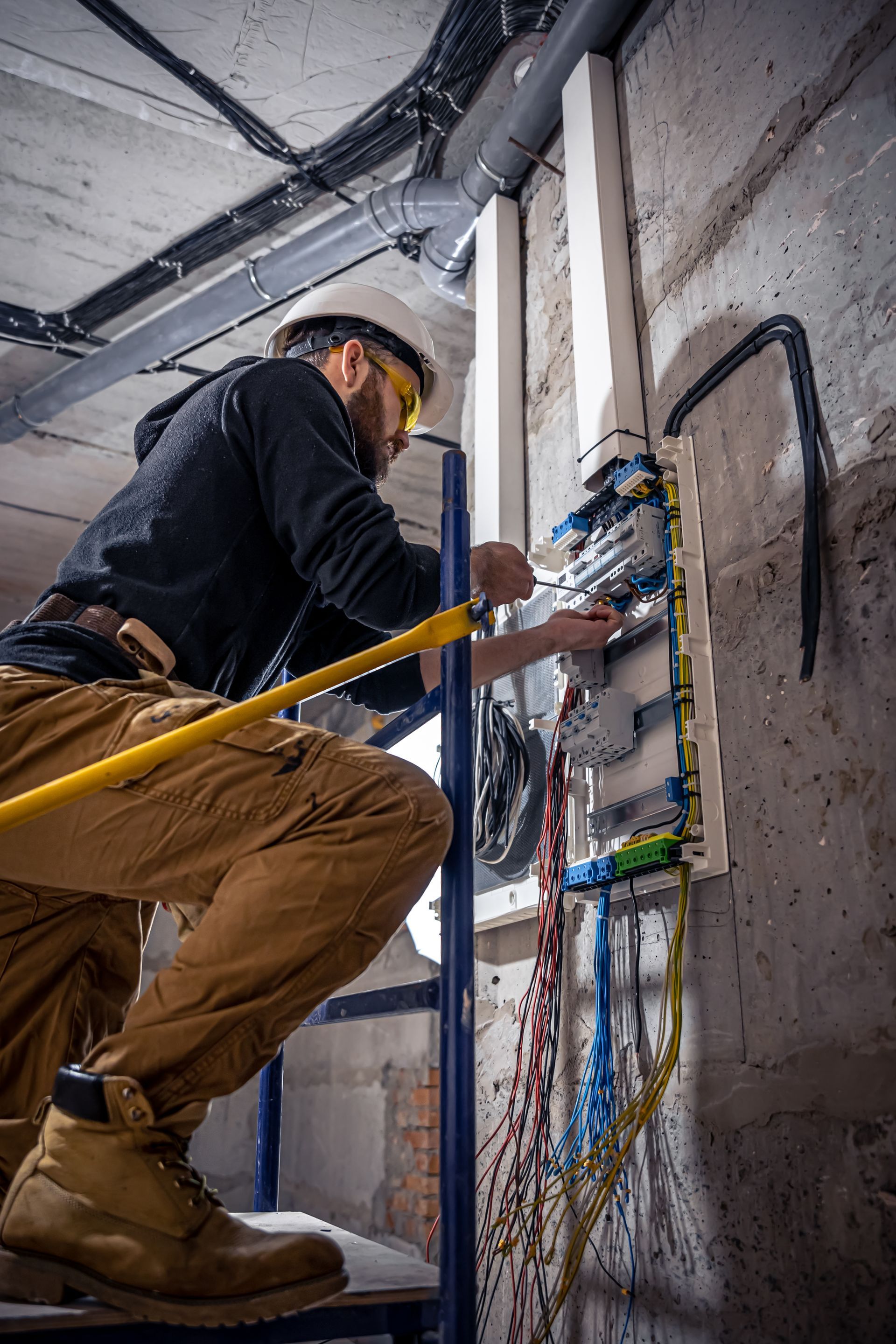 A man is kneeling on a ladder working on an electrical box.