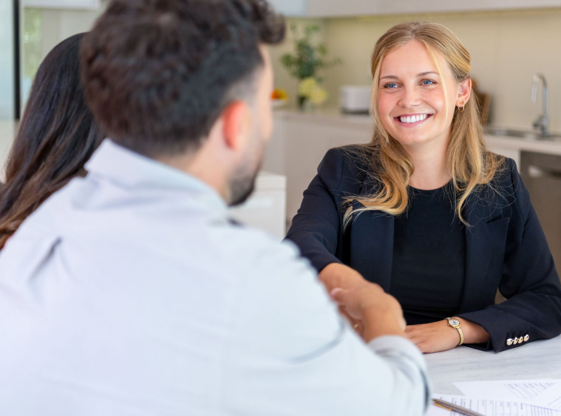 Two people in a bright office smiling and shaking hands across a table