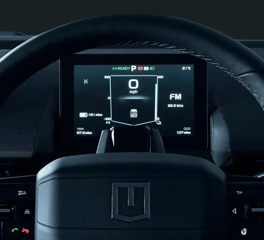 Steering wheel and digital dashboard of an electric vehicle showing speed, battery range, and radio status.
