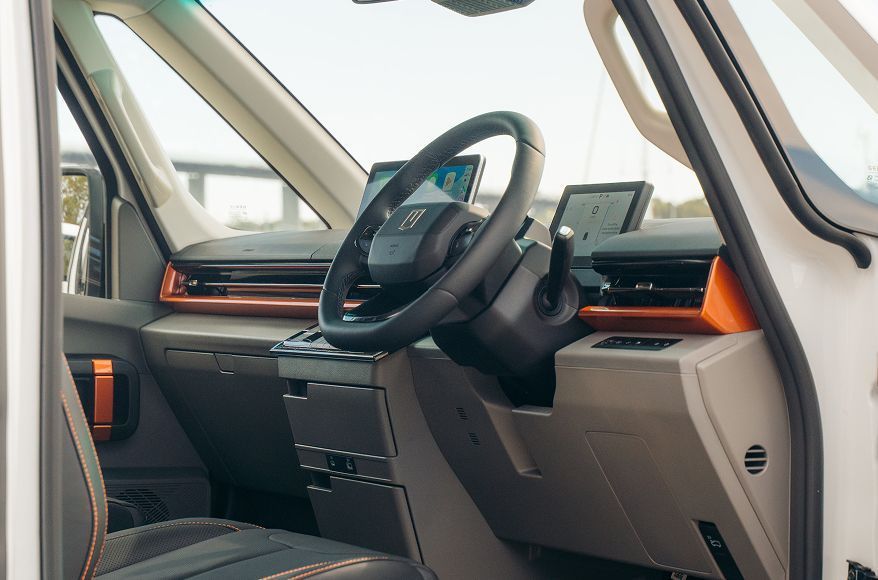 The interior view of a modern vehicle, featuring a black steering wheel, digital dashboard, and orange trim accents.