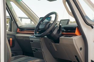 The interior of a modern, light-colored vehicle, featuring a black steering wheel, digital dashboard, and orange accents.