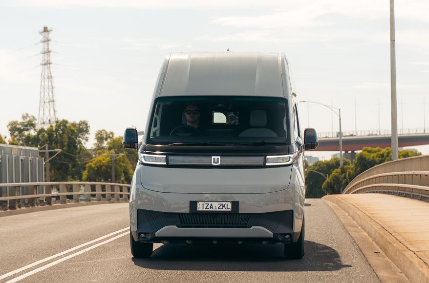 A grey electric delivery van driving forward on a bridge during the day.