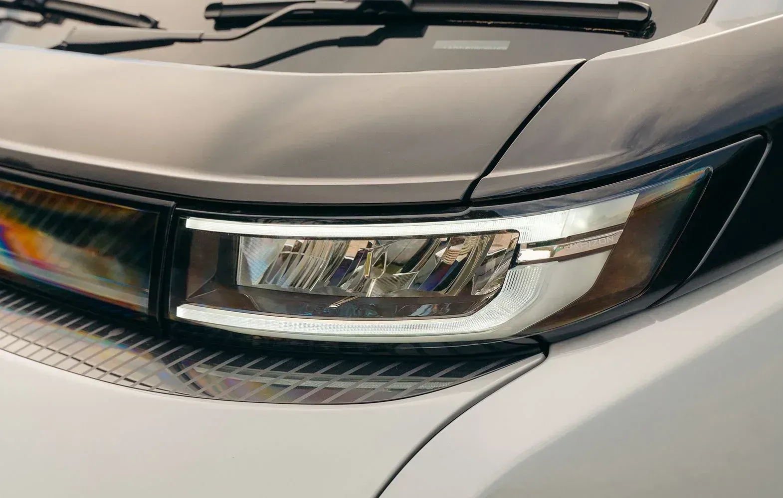 Close-up of a modern car's sleek, rectangular LED headlight assembly with silver trim and a dark gray hood and body.