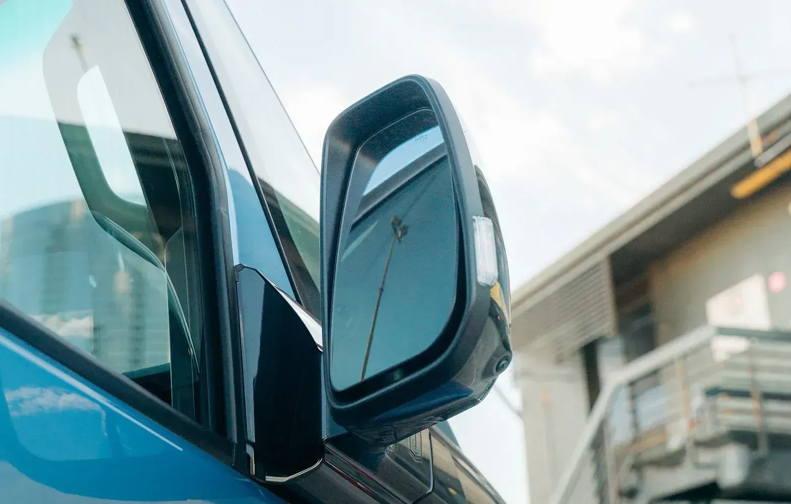Side-view mirror of a bright blue vehicle, reflecting a tall utility pole and a building.
