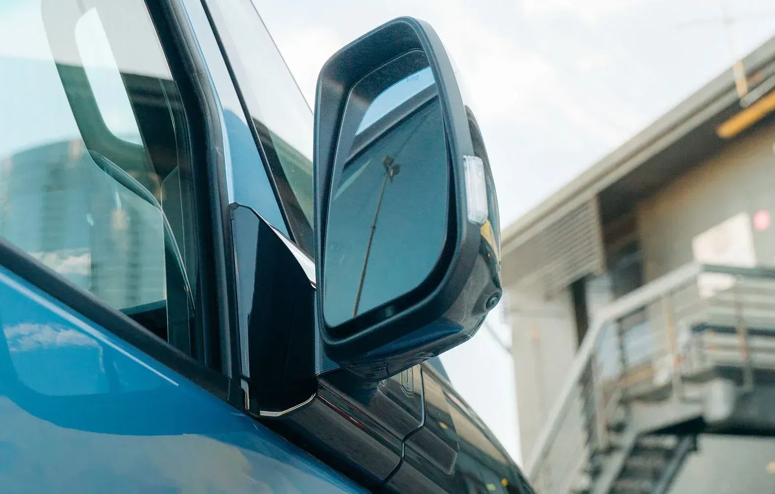 Close-up of a blue vehicle's side mirror and window, with a building blurred in the background.
