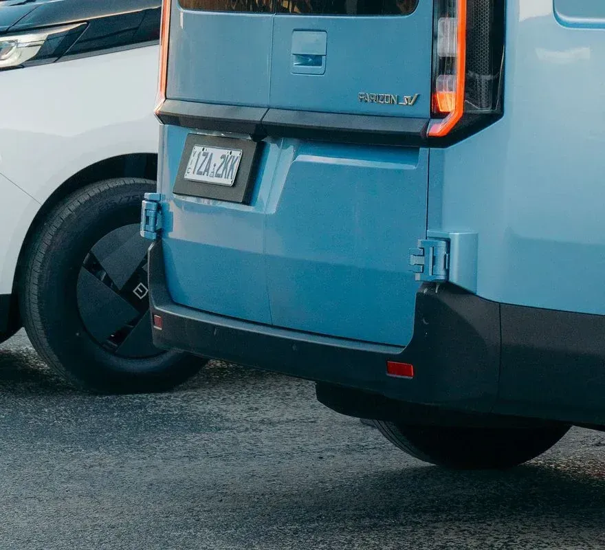 A light blue cargo van parked next to a white car on an asphalt surface.
