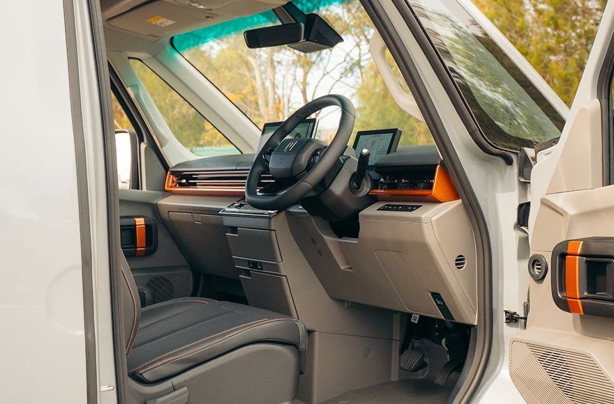 Interior of a modern van with grey seats, orange accents, a black steering wheel, and digital dashboard displays.