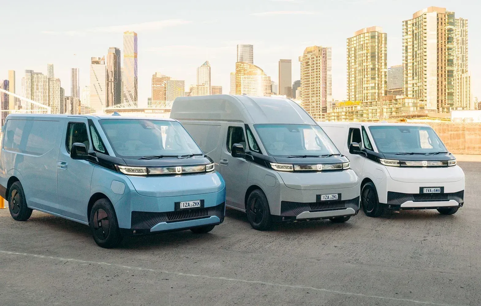 Three vans in blue, gray, and white parked in a row with a city skyline in the background.