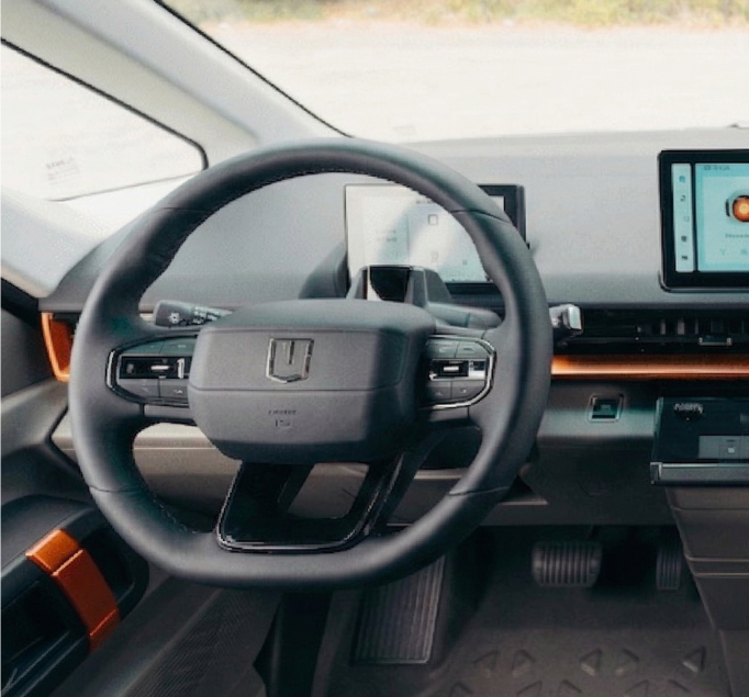 Modern car interior with a black leather steering wheel, digital dashboard screen, and orange accents on the trim.
