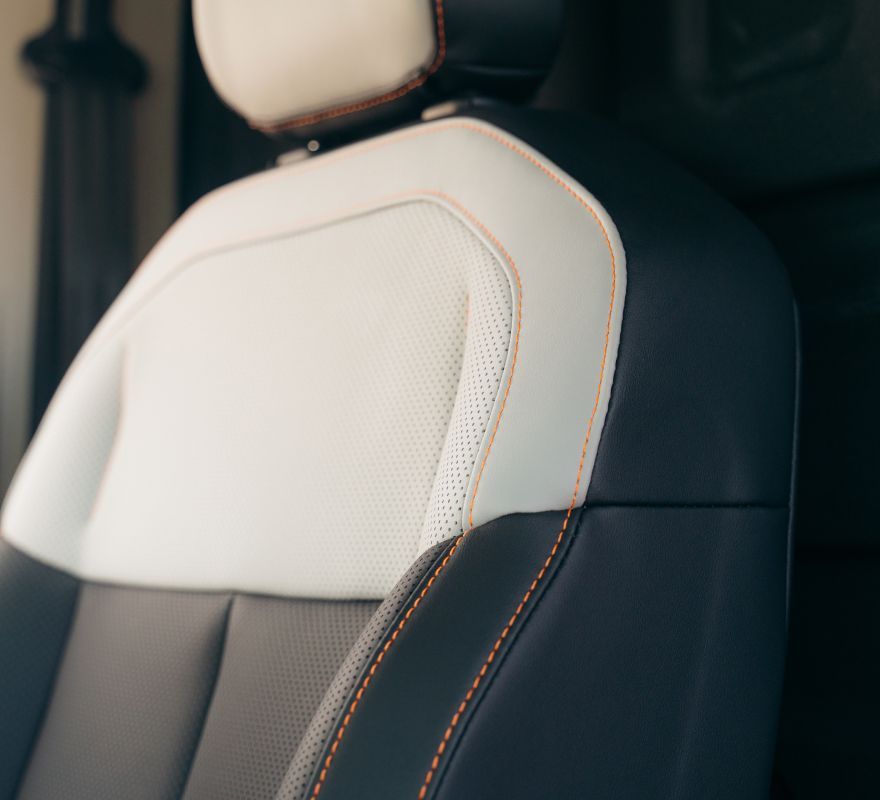 A car seat featuring a two-tone design of white perforated leather and black side panels with orange accent stitching.