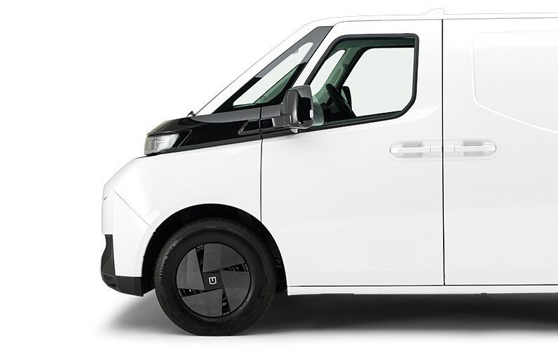 A white commercial van seen from the side, focusing on the front cabin, wheel, and door.