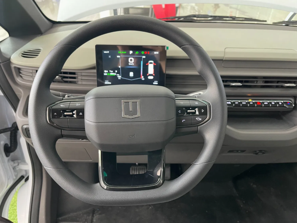 A view from the driver's seat of a vehicle, focusing on the dark grey steering wheel and the digital instrument cluster.