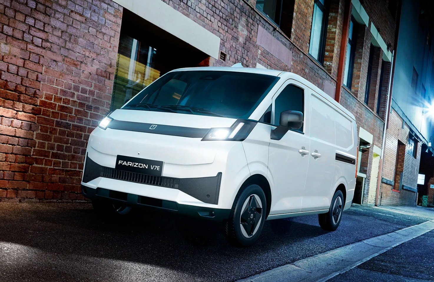 A white electric van parked on a cobblestone street next to a brick building.