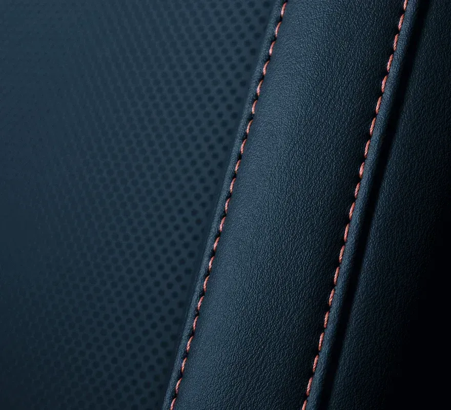 A close-up of dark textured leather upholstery featuring two parallel rows of contrasting orange stitched seams.
